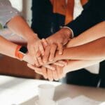 Dłonie różnorodnego zespołu złożone razem nad białym biurkiem